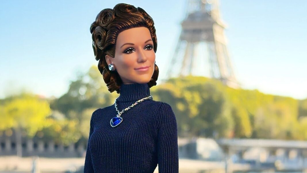 Lacivert balıkçı yaka elbise ve mavi kalp kolye takan Celine Dion Barbie bebeği, arka planda Eyfel Kulesi