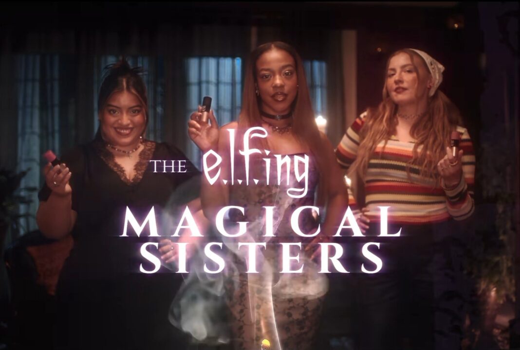 Koyu renkli, mum ışıklı bir odada makyaj ürünleri tutan üç genç kadın ve “The e.l.f.ing Magical Sisters” yazısı