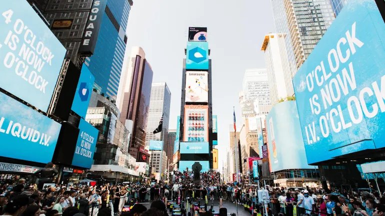 Times Square’de Liquid I.V. reklamlarının yer aldığı mavi dijital ekranlar ve meydandaki kalabalık