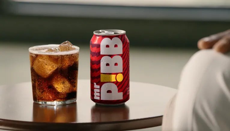 Masa üzerinde buzlu bir bardak gazlı içecek ve yanında kırmızı Mr. Pibb kutusu