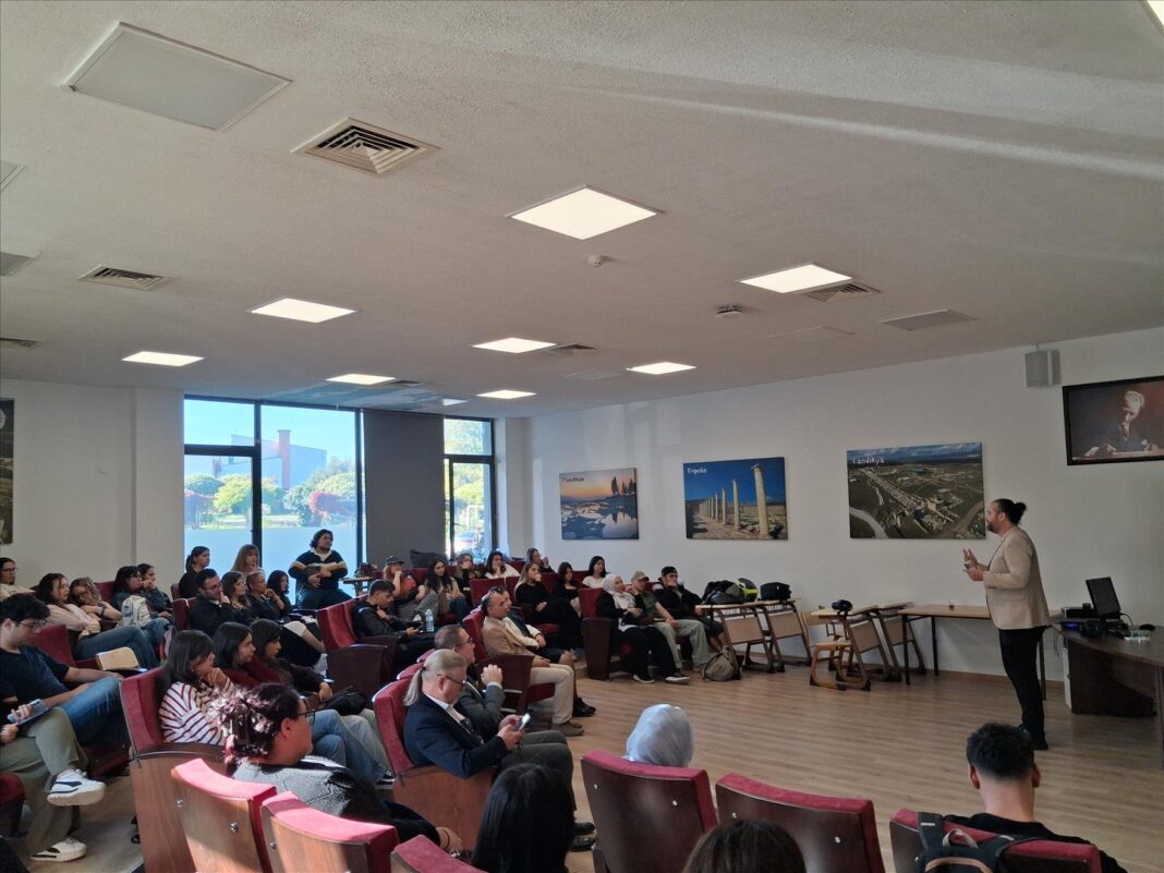 Pamukkale Üniversitesi İletişim Fakültesi’ndeki Kariyer Buluşmaları etkinliğinde salonda oturan öğrenciler ve sağda ayakta konuşan bir kişi
